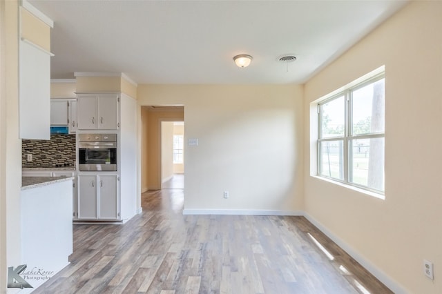 kitchen featuring backsplash, light wood-type flooring, light countertops, white cabinets, and stainless steel oven