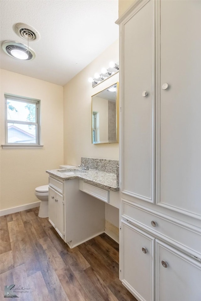 bathroom featuring toilet, baseboards, wood finished floors, and vanity