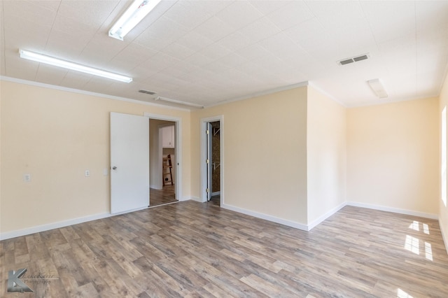 empty room with visible vents, ornamental molding, and wood finished floors