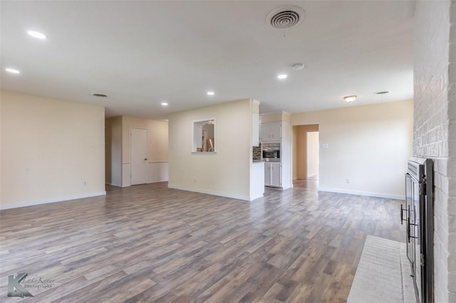 unfurnished living room with a fireplace, recessed lighting, wood finished floors, and visible vents