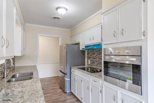 kitchen featuring crown molding, white cabinetry, under cabinet range hood, a sink, and stainless steel appliances