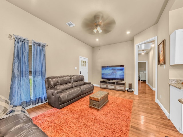 living room with visible vents, a ceiling fan, light wood finished floors, and baseboards