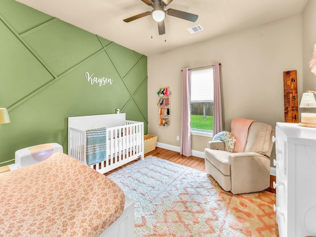 bedroom with a crib, light wood finished floors, a ceiling fan, baseboards, and visible vents