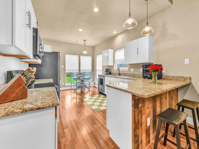 kitchen with white cabinets, appliances with stainless steel finishes, light wood finished floors, a kitchen breakfast bar, and recessed lighting