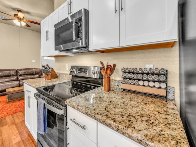 kitchen featuring white cabinets, light stone counters, a ceiling fan, light wood-style flooring, and appliances with stainless steel finishes