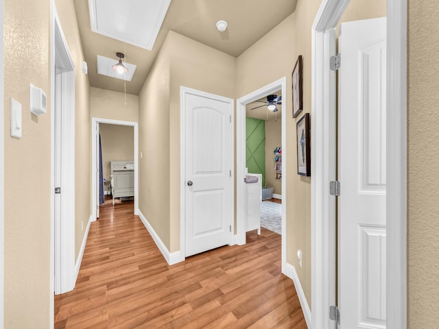 hall featuring light wood-type flooring, attic access, and baseboards