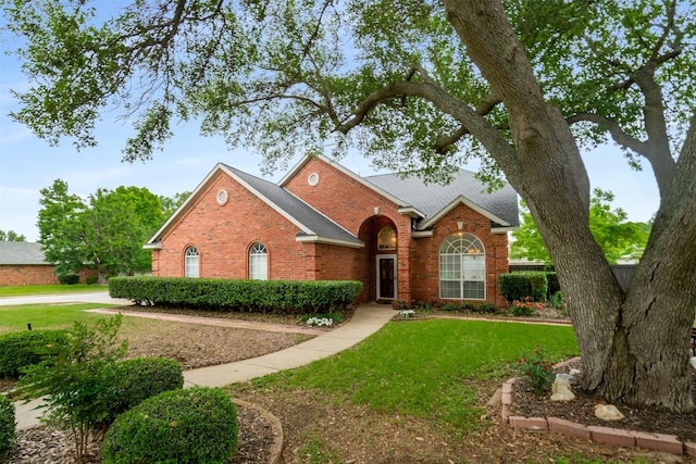 view of front facade with brick siding, a front lawn, and roof with shingles