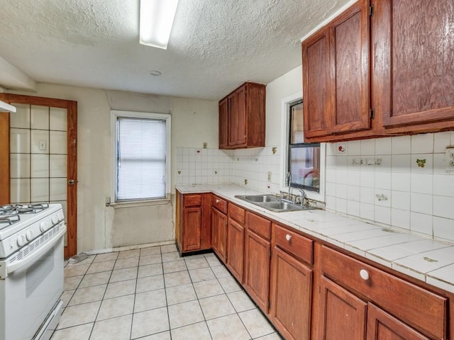 4942 Terry St, Dallas, TX 75223 - kitchen featuring decorative backsplash, a textured ceiling, a sink, light tile patterned floors, and white range with gas stovetop