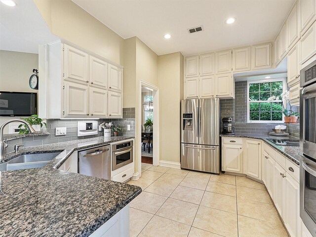 kitchen with stainless steel appliances, a sink, decorative backsplash, dark stone countertops, and recessed lighting