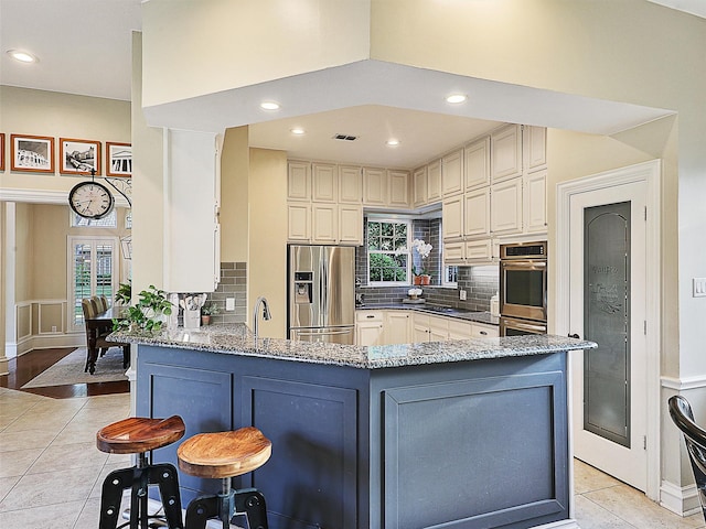 kitchen with stainless steel appliances, light stone countertops, a peninsula, light tile patterned floors, and backsplash