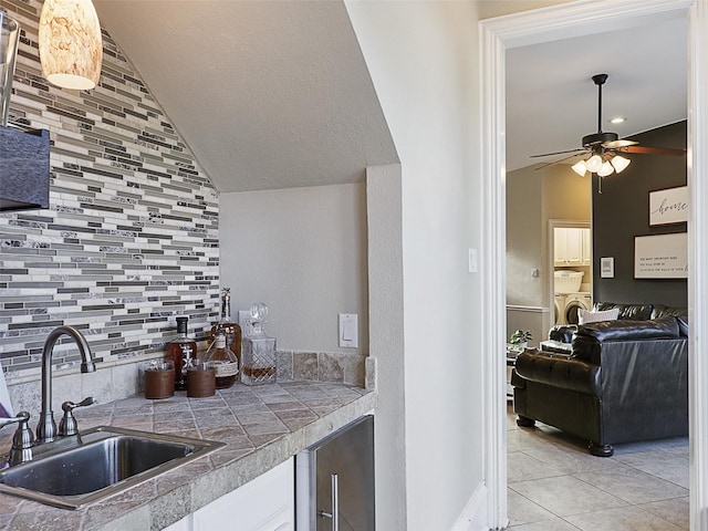kitchen with vaulted ceiling, a sink, washer and dryer, light tile patterned floors, and tasteful backsplash