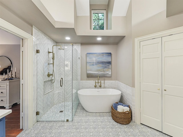 full bathroom featuring tile walls, a stall shower, a soaking tub, a wainscoted wall, and vanity