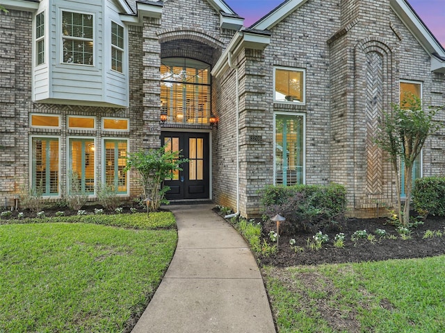doorway to property featuring french doors, brick siding, and a lawn