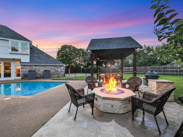 pool at dusk with an outdoor fire pit, central AC unit, a patio area, and a fenced backyard