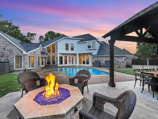 pool at dusk with a fire pit, cooling unit, a patio, and fence