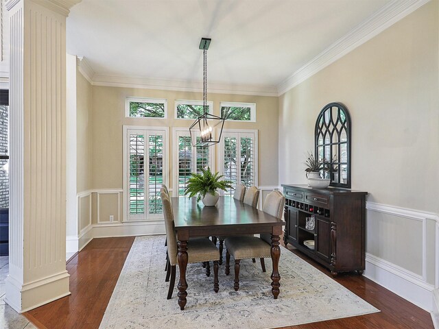 dining area with dark wood-style floors, ornamental molding, a wainscoted wall, a chandelier, and a decorative wall