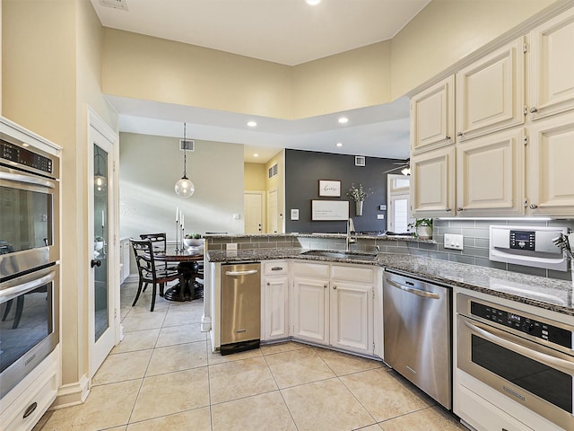 kitchen with appliances with stainless steel finishes, a sink, light tile patterned flooring, a peninsula, and dark stone countertops
