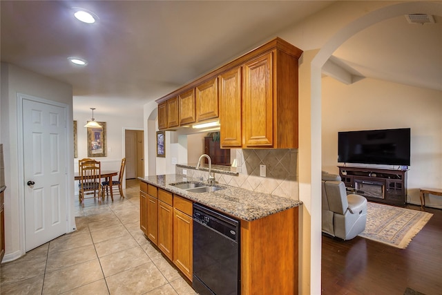 kitchen with backsplash, arched walkways, light stone countertops, dishwasher, and a sink