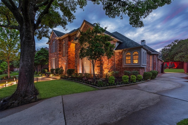 property exterior at dusk featuring brick siding, driveway, and a chimney