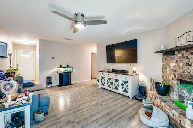 living area featuring a fireplace, light wood-style floors, a ceiling fan, baseboards, and visible vents