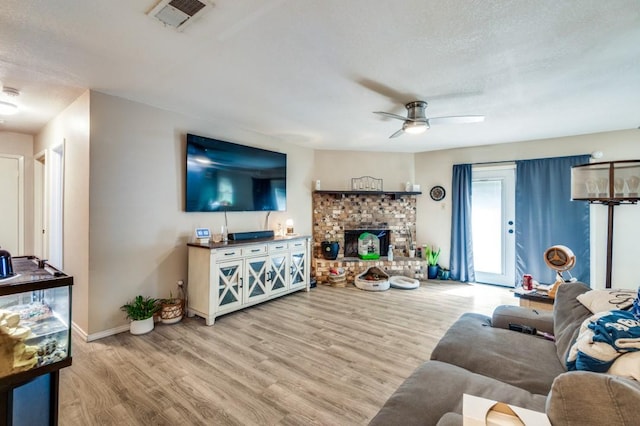 living room with visible vents, wood finished floors, baseboards, a stone fireplace, and a ceiling fan