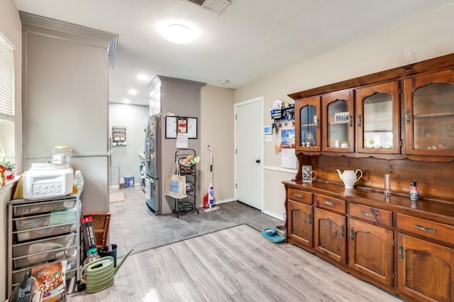 interior space featuring brown cabinetry, visible vents, dark countertops, glass insert cabinets, and light wood-style floors