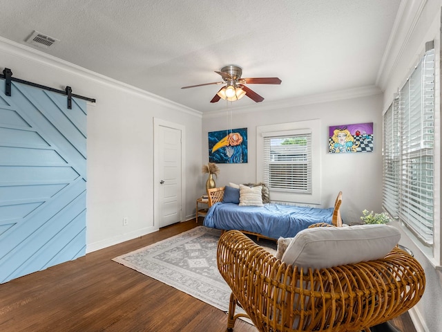 bedroom with visible vents, a barn door, crown molding, and wood finished floors