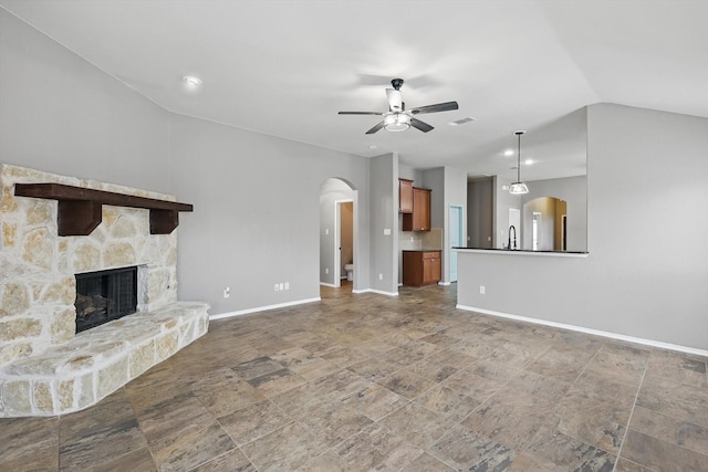 unfurnished living room with a ceiling fan, stone finish flooring, arched walkways, vaulted ceiling, and baseboards