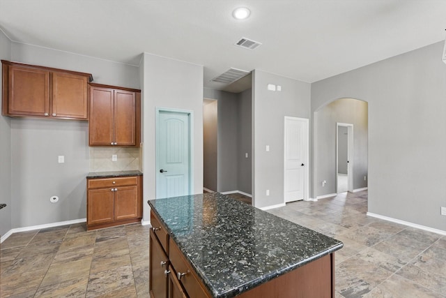 kitchen with arched walkways, baseboards, visible vents, and stone finish floor