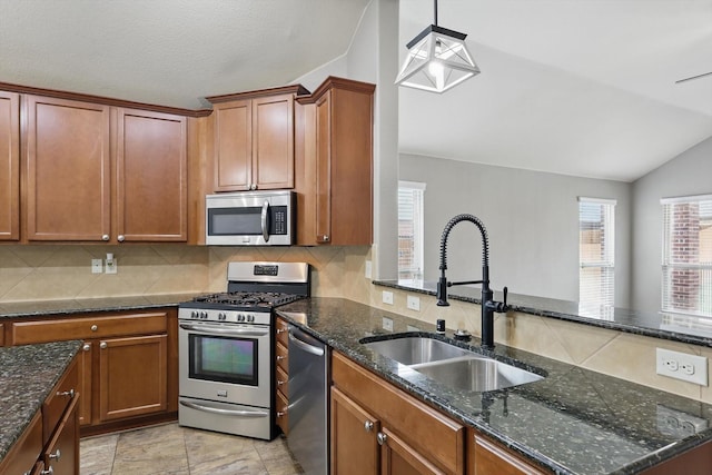 kitchen with decorative backsplash, appliances with stainless steel finishes, a sink, lofted ceiling, and dark stone counters