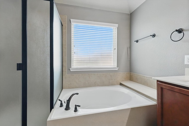 full bath featuring a textured wall, walk in shower, a garden tub, and vanity