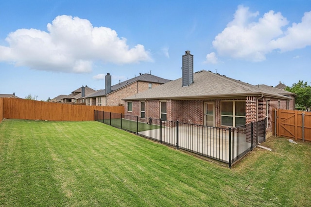 rear view of house featuring a fenced backyard, roof with shingles, a chimney, brick siding, and a lawn