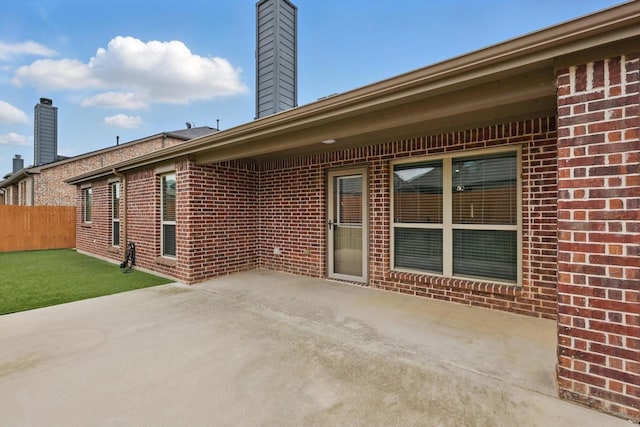 rear view of property featuring fence, a chimney, a patio area, and brick siding