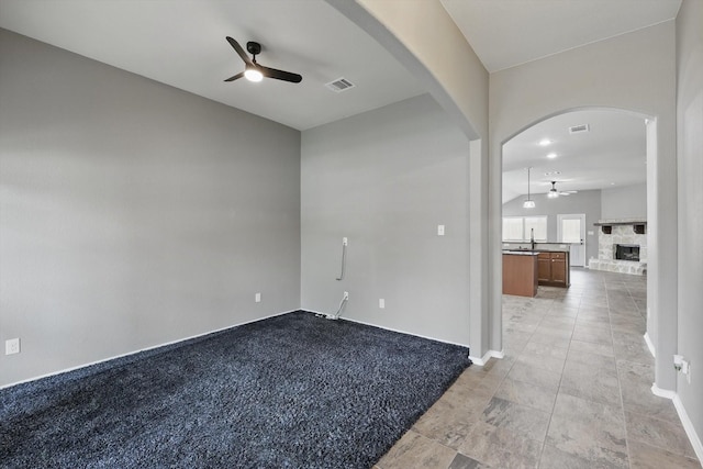 spare room featuring arched walkways, ceiling fan, a fireplace with raised hearth, and visible vents