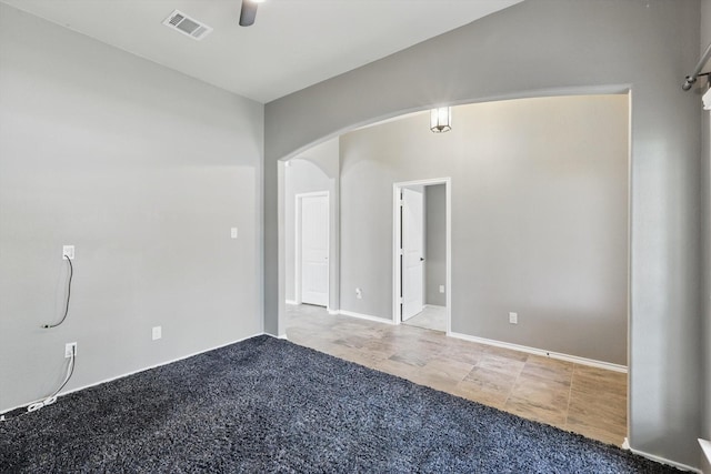 empty room featuring arched walkways, a ceiling fan, visible vents, and baseboards
