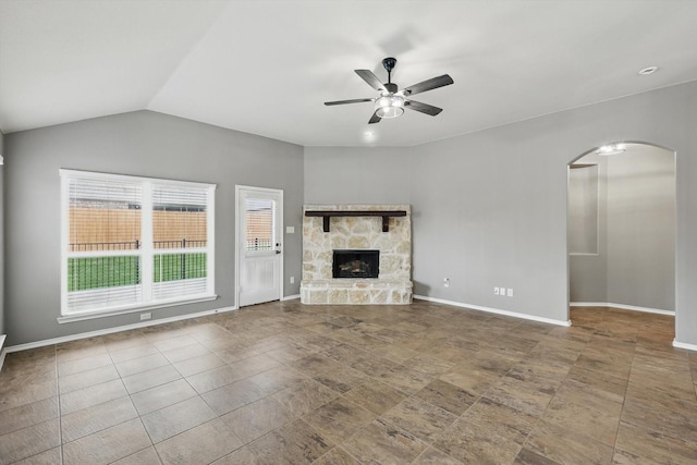 unfurnished living room featuring arched walkways, a ceiling fan, a stone fireplace, and baseboards