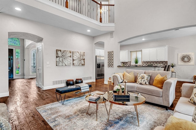 living room featuring visible vents, arched walkways, baseboards, and a high ceiling