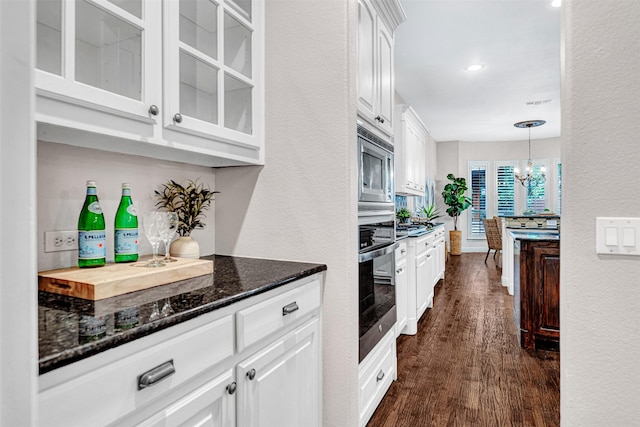 kitchen with a chandelier, dark stone countertops, stainless steel appliances, white cabinetry, and glass insert cabinets
