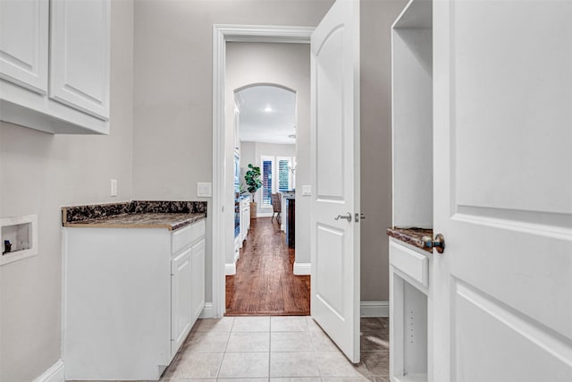 clothes washing area featuring washer hookup, arched walkways, cabinet space, baseboards, and light tile patterned flooring