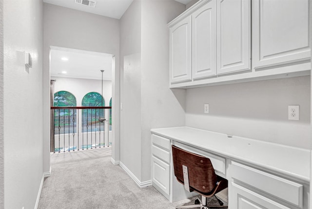unfurnished office with baseboards, built in desk, visible vents, and light carpet