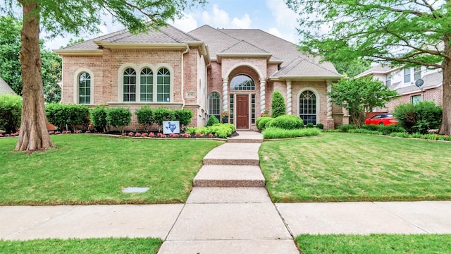 view of front of house with brick siding, a front yard, and roof with shingles
