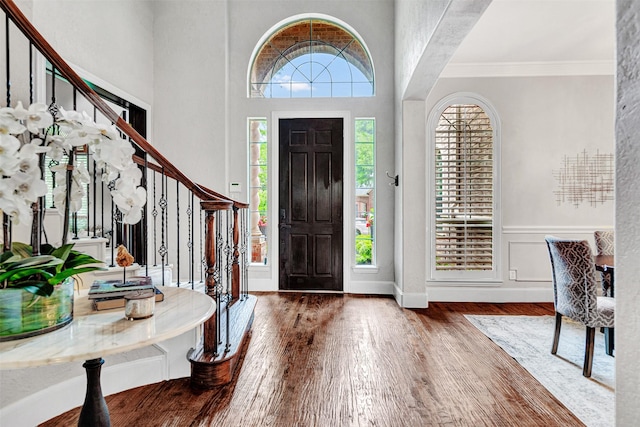 foyer with stairway, a wainscoted wall, ornamental molding, and wood finished floors