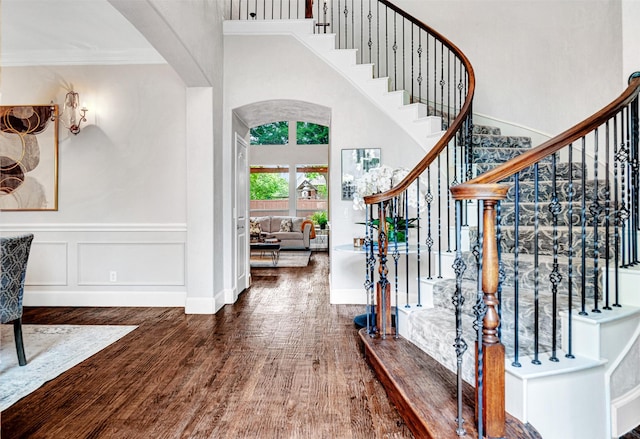 foyer entrance featuring crown molding, arched walkways, stairs, and wood finished floors