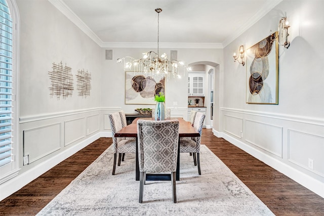 dining room featuring arched walkways, a chandelier, ornamental molding, a decorative wall, and dark wood-type flooring