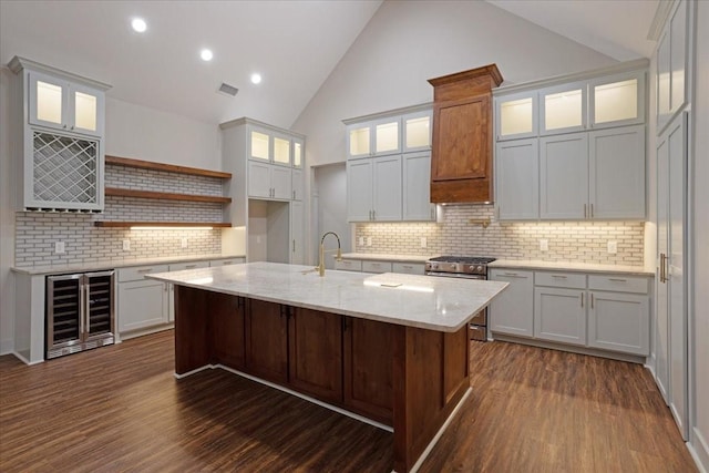 kitchen with dark wood-type flooring, wine cooler, a kitchen island with sink, and tasteful backsplash