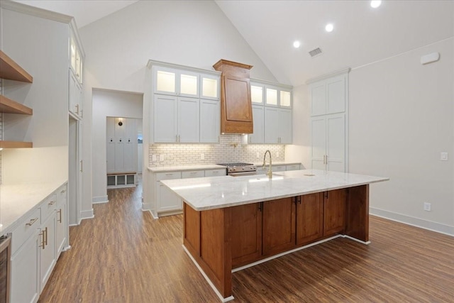 kitchen featuring backsplash, dark wood-style flooring, visible vents, a center island with sink, and high vaulted ceiling