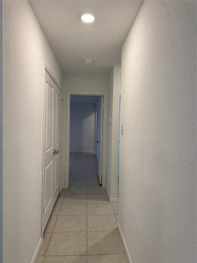 hall featuring baseboards, a textured wall, and light tile patterned floors