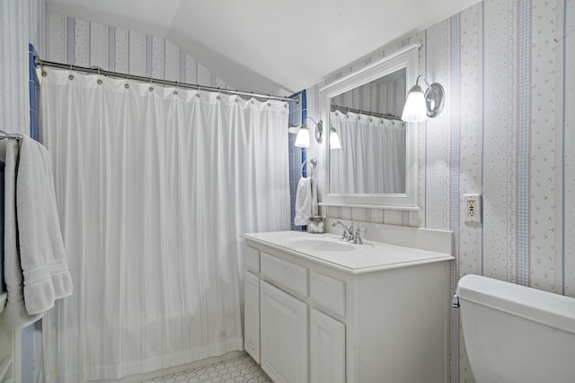 full bathroom featuring toilet, wallpapered walls, lofted ceiling, and vanity