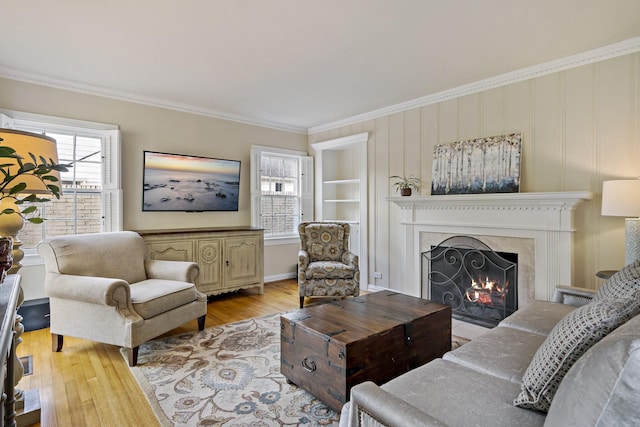 living area with crown molding, built in shelves, light wood-style flooring, and a high end fireplace