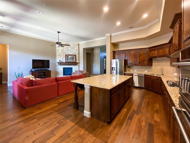 kitchen with a center island, stainless steel appliances, a ceiling fan, dark wood-type flooring, and ornamental molding
